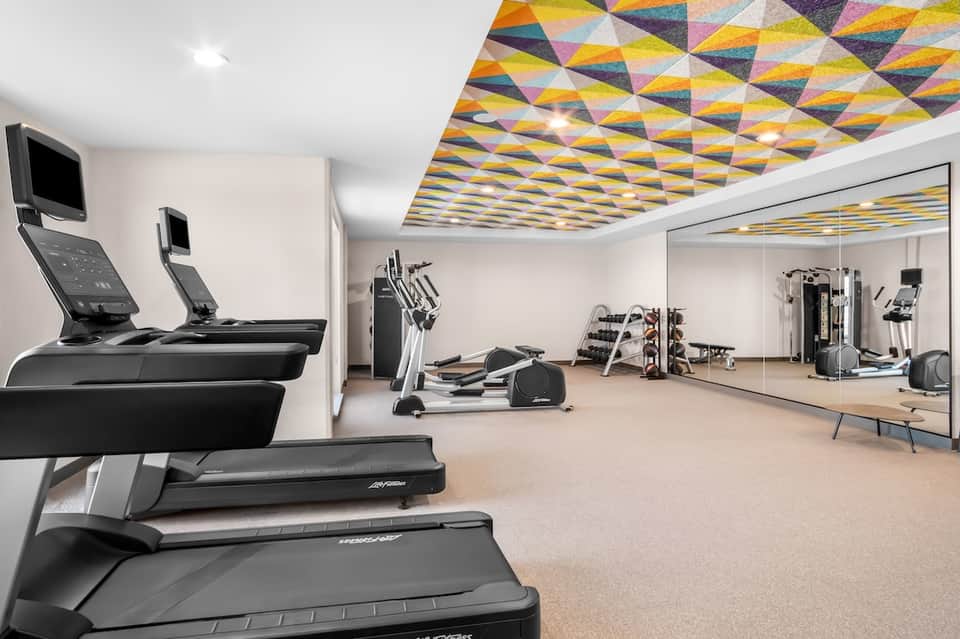 Spacious gym with colorful geometric ceiling, multiple treadmills, and mirrored walls