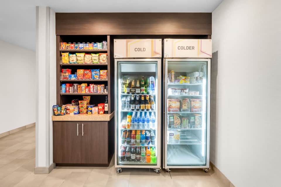Hotel pantry with snack shelves and two glass-door refrigerators stocked with beverages and food