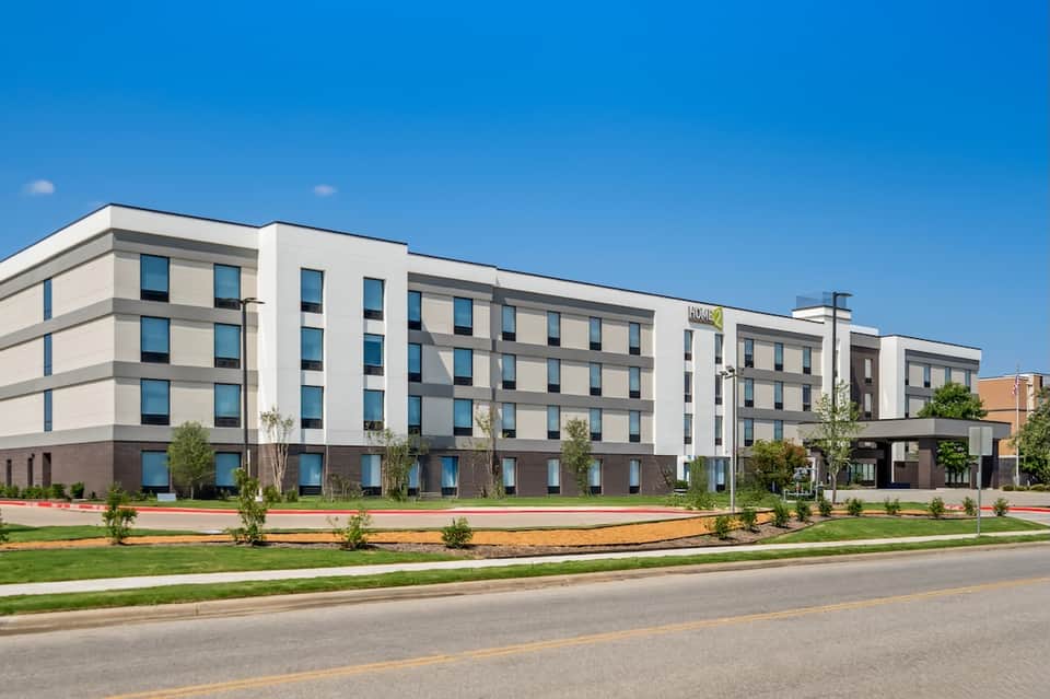 Modern hotel building with cream and brown facade, manicured landscape, and clear blue sky