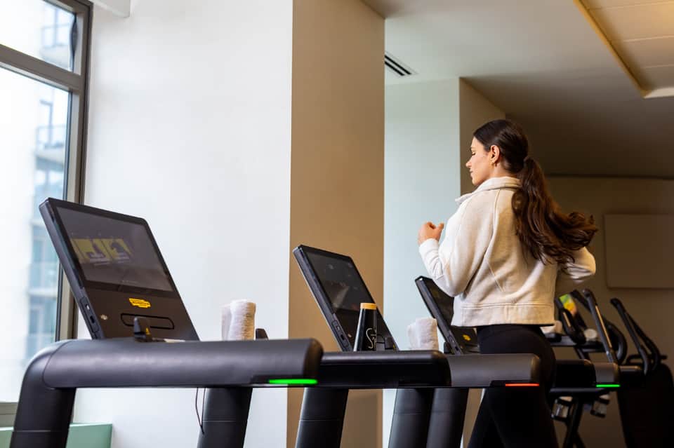 Woman exercising on treadmill in bright modern gym with large windows and contemporary equipment