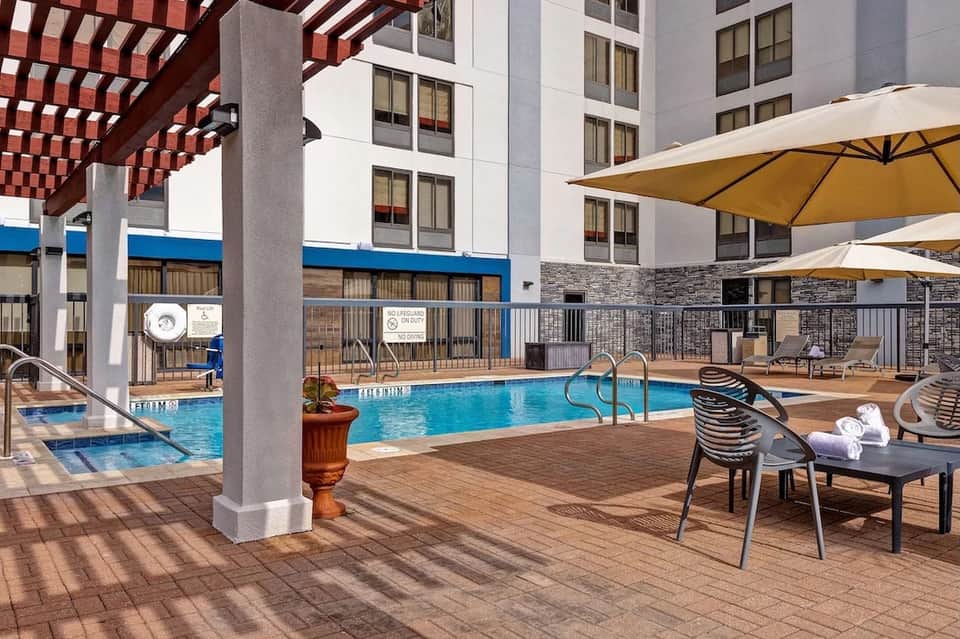 Resort pool area with red pergola, umbrellas, loungers, and modern building architecture