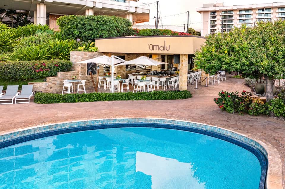 Poolside restaurant terrace with white umbrellas, dining tables, and lush greenery
