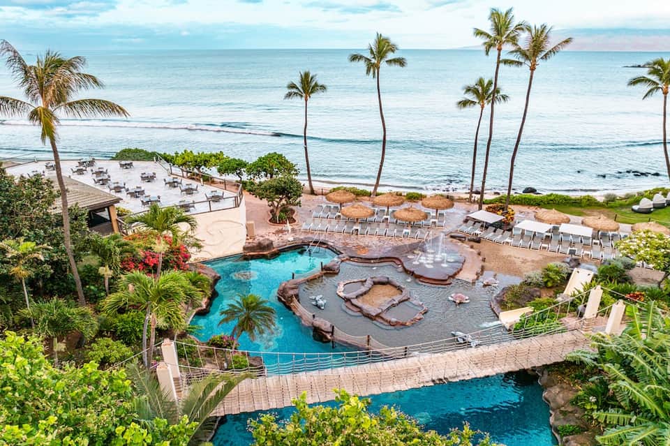 Beachfront resort pool complex with hot tubs, palm trees, ocean views, and multiple lounge areas
