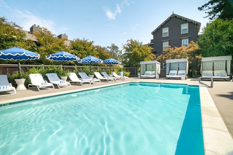 Hotel pool with white lounge chairs, blue umbrellas, and historic mansion in background
