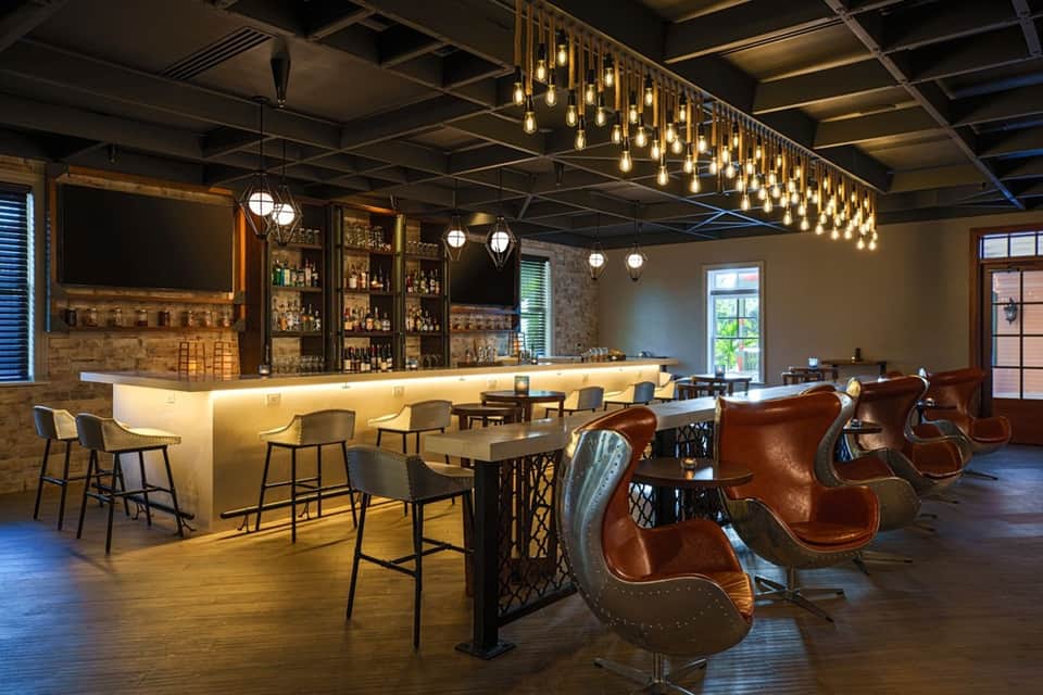 Upscale hotel bar with leather chairs, brick wall, brass fixtures, and hanging lights