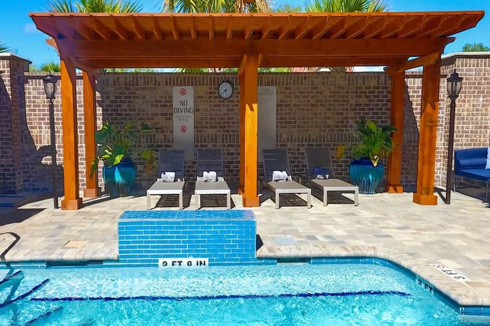 Poolside cabana with orange pergola, white loungers, and brick privacy wall