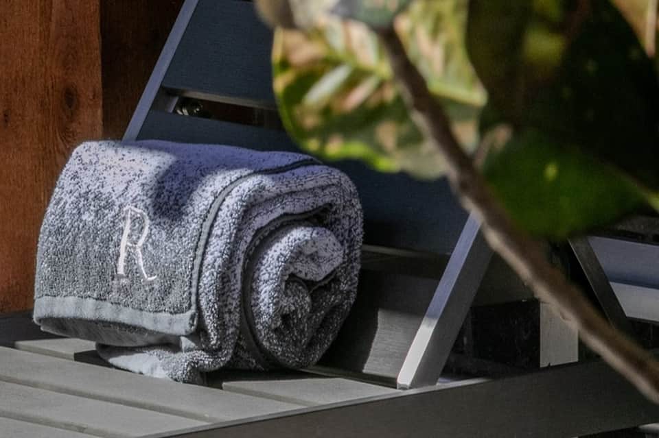 Rolled gray towel with monogram on lounge chair beside plant