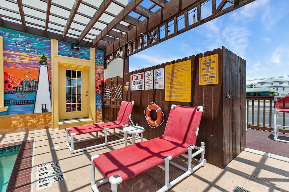 Beachfront resort deck with colorful lifeguard station, red loungers, and poolside cabanas