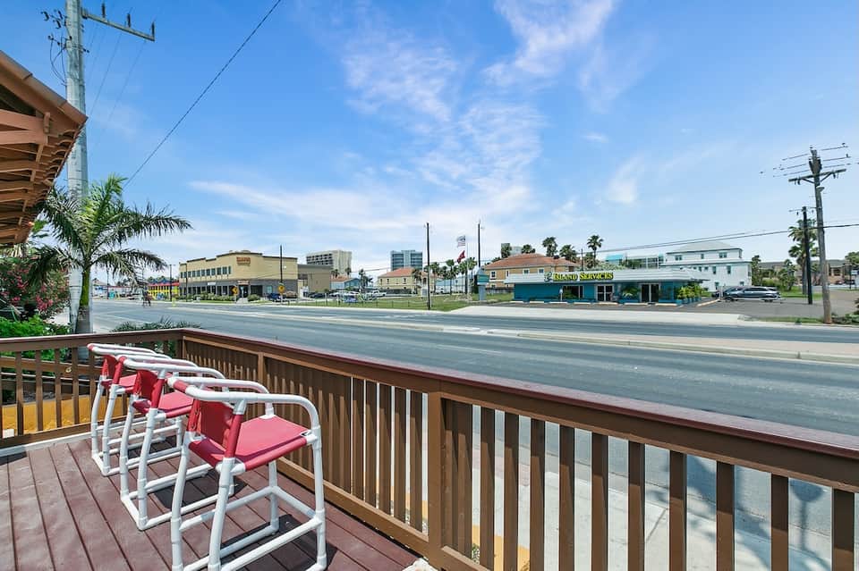 Waterfront deck with red and white lounge chairs overlooking bay with palm trees and buildings