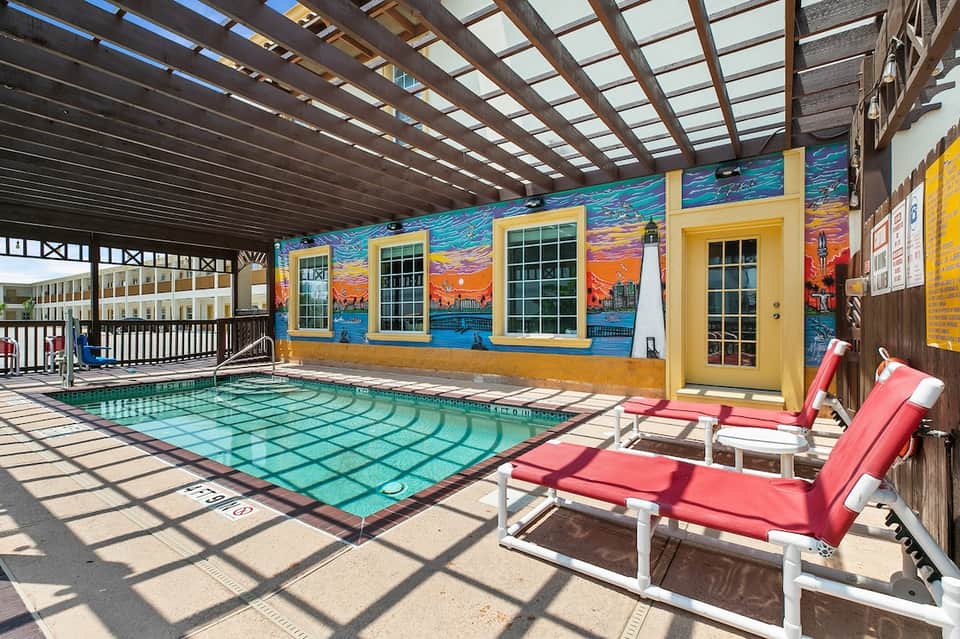 Covered indoor pool with colorful murals, red lounge chairs, and natural skylights