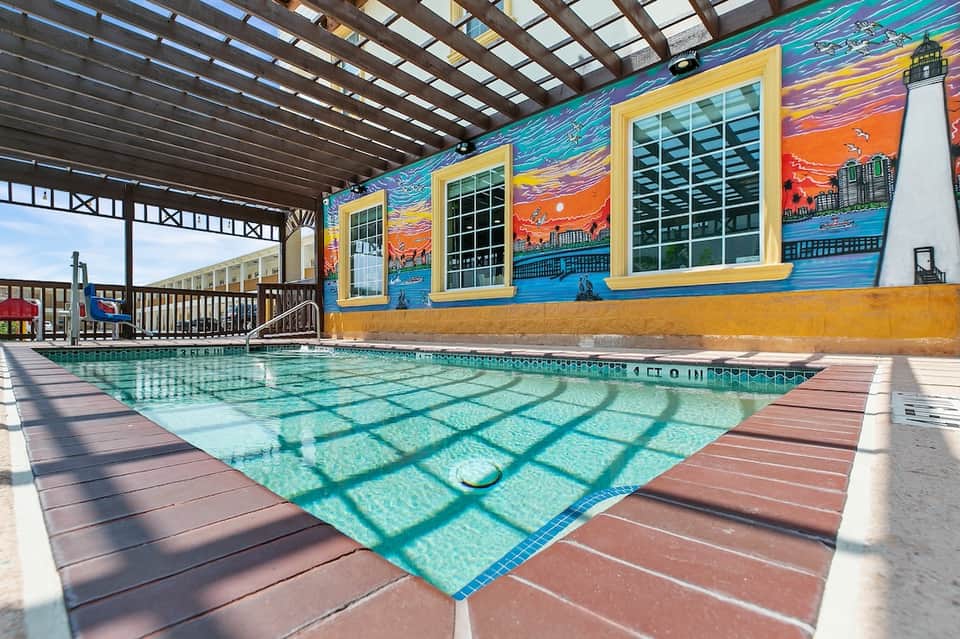 Covered indoor pool with colorful lighthouse mural, wooden deck, and seaside-themed wall art