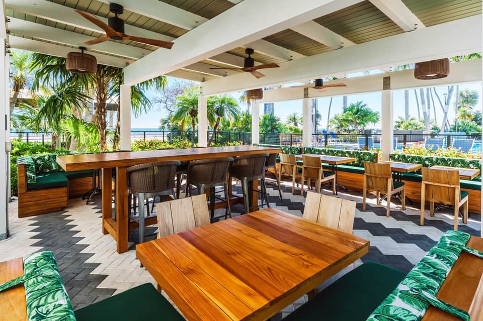 Covered dining pavilion with wooden tables, ocean views, and tropical plants