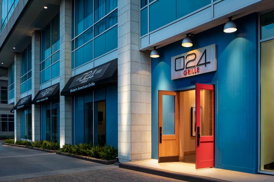 Modern restaurant storefront with blue exterior, orange door, and neon signage