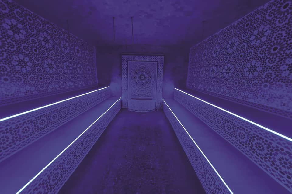 Purple-lit hammam spa corridor with ornate Moroccan tilework and glowing neon accent lighting