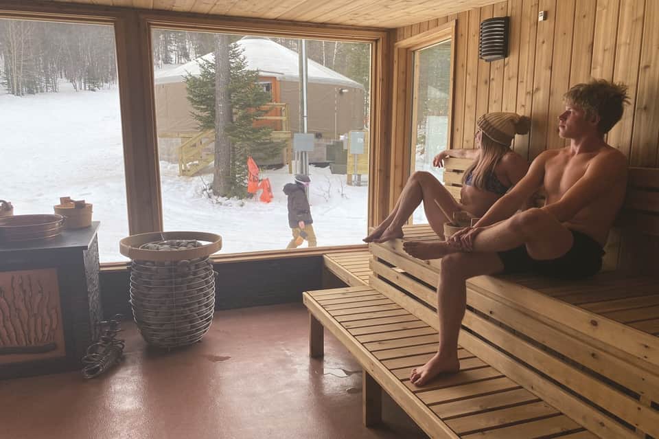 Sauna interior with wooden benches and large windows overlooking snowy winter landscape