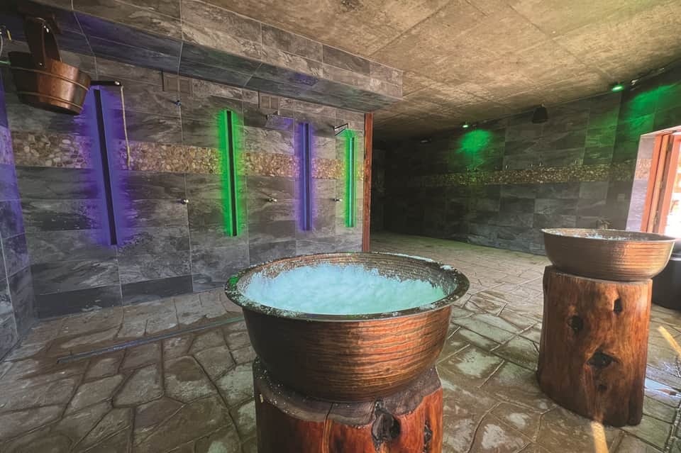 Modern spa hot tub room with stone walls, colorful neon accent lighting, and wooden soaking tubs