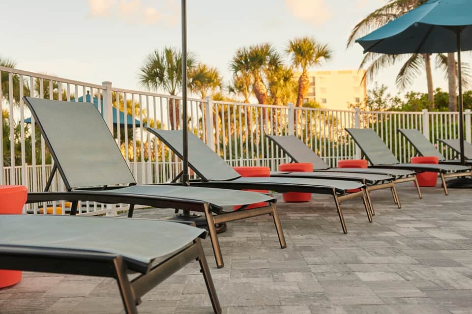 Beachfront deck with lounge chairs, red cushions, umbrellas, and palm tree views at golden hour