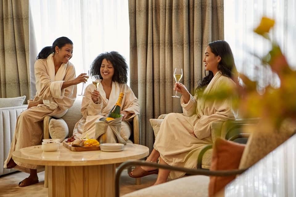 Three women in spa robes celebrating with champagne in luxurious hotel room