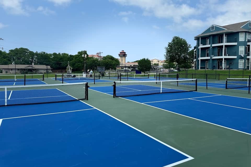 Multiple blue and green tennis courts with white lines and nets, residential building visible in background