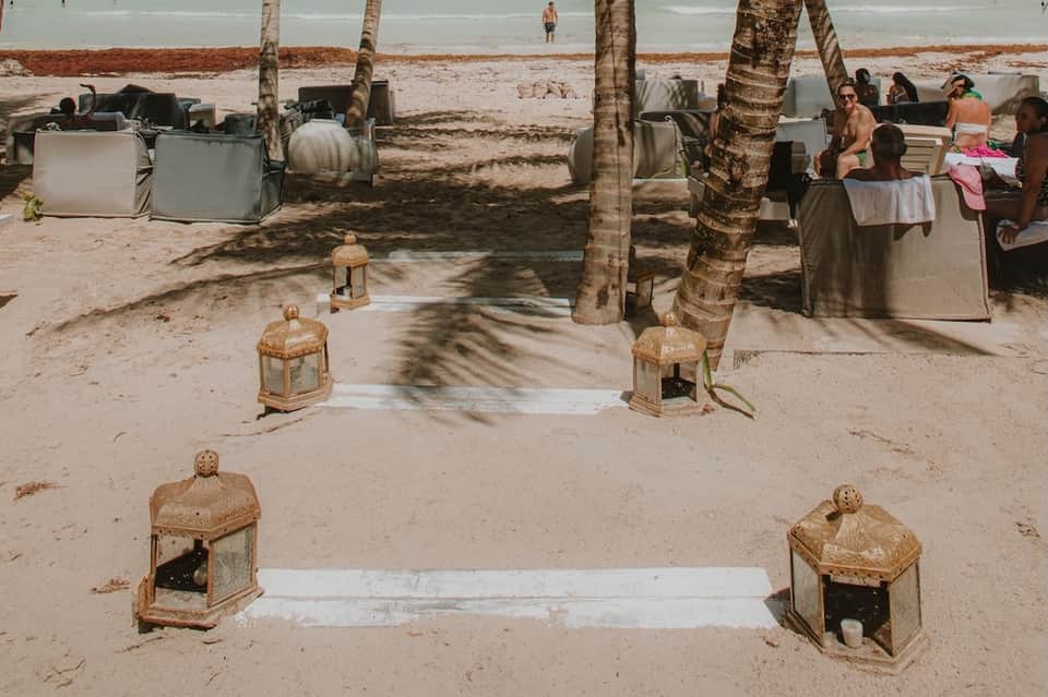 Beach gathering with palm trees, seating areas, and people relaxing near shoreline