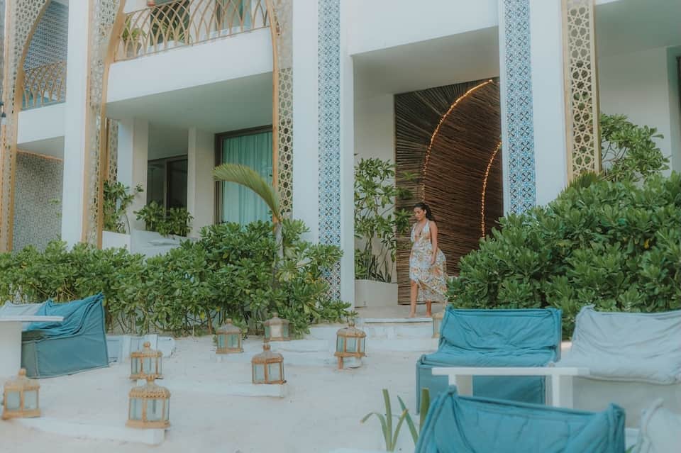 Beachfront resort with white architecture, decorative lattice screens, blue loungers, and tropical plants