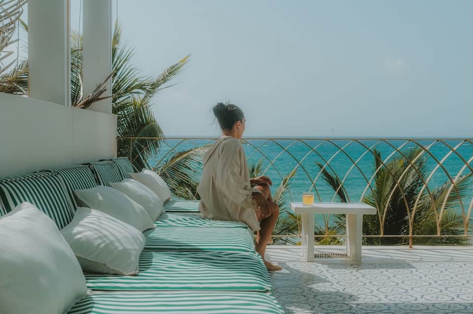 Woman relaxing on striped daybed on ocean-view terrace with palm trees and railing