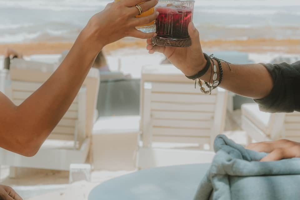 Two people toasting with red cocktails on a beach cabana overlooking the ocean