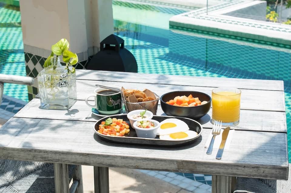Poolside breakfast table with eggs, fresh fruit, juice, and flowers