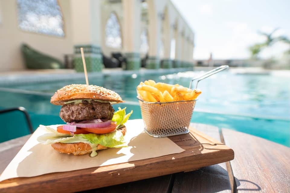 Gourmet burger and fries served poolside with resort architecture and water features