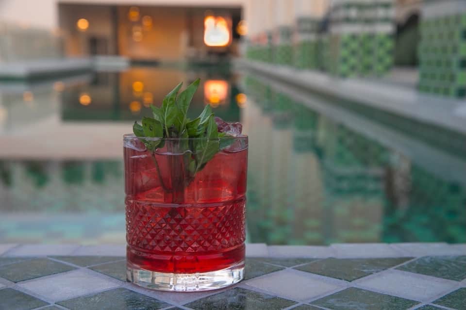 Red cocktail with mint garnish on outdoor terrace at dusk with glowing resort lights