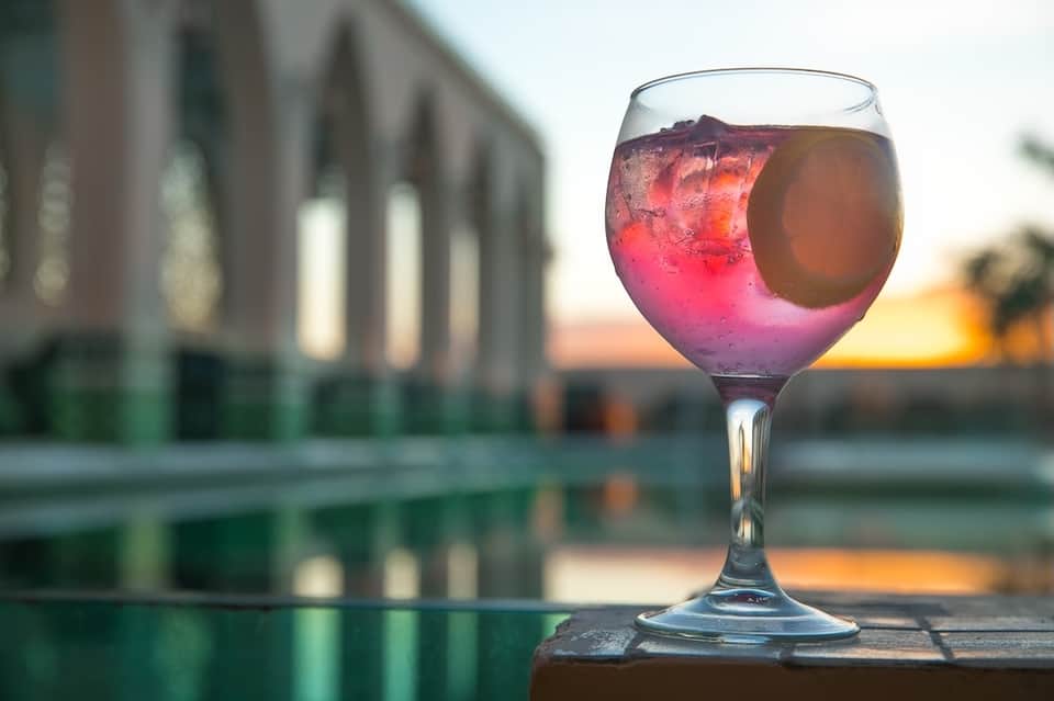 Pink cocktail in glass against sunset with waterfront building reflection in background