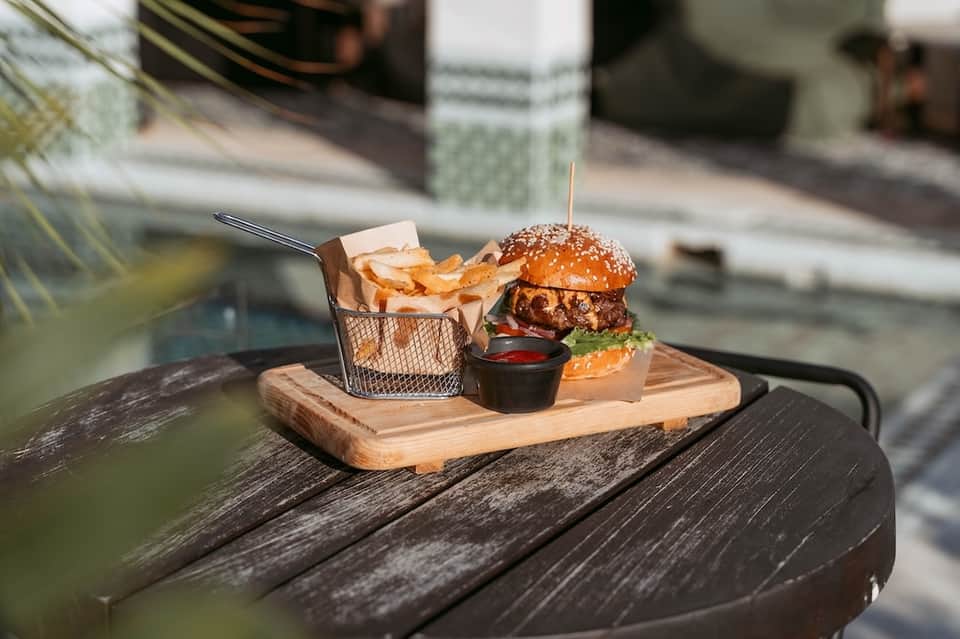 Gourmet burger with fries served on wooden board poolside with beverage