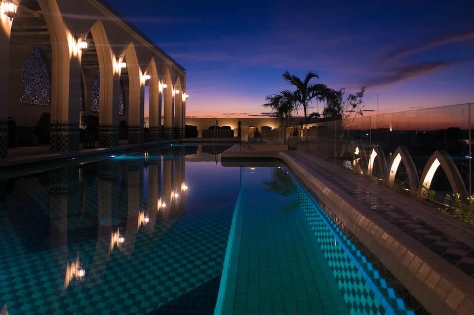 Elegant poolside area at dusk with lit archways, reflecting pool, and palm trees