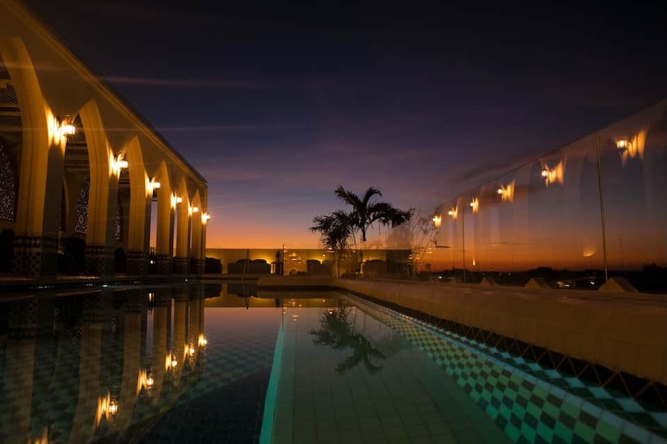 Illuminated infinity pool at dusk reflecting golden lights with palm tree and modern architecture