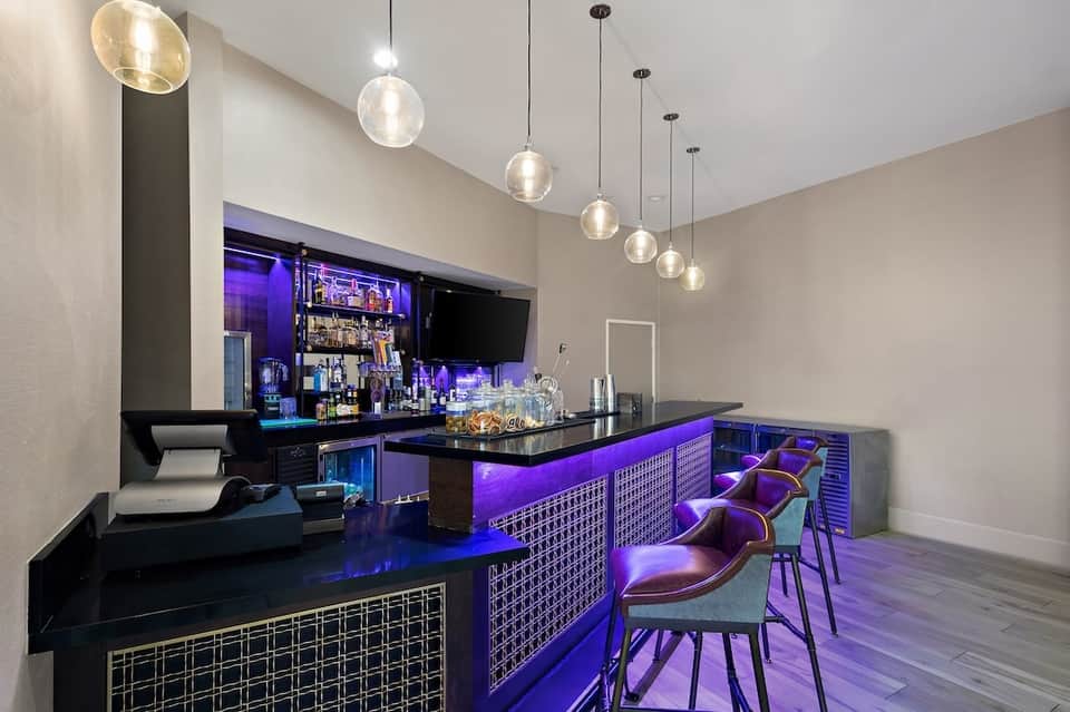 Modern hotel bar with purple lighting, black counters, pendant lights, and barstool seating