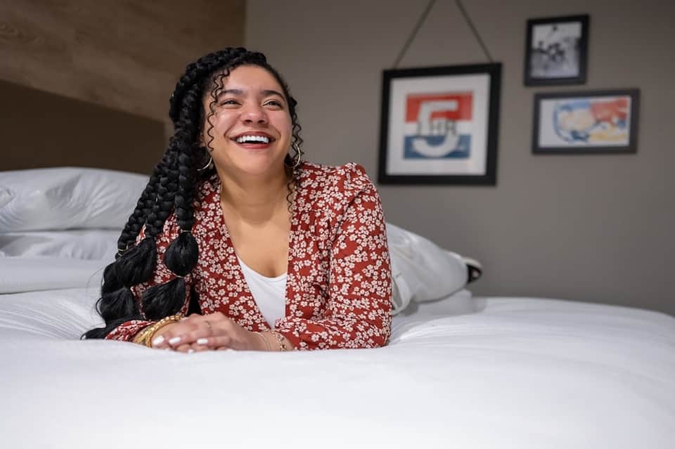 Smiling woman on comfortable white bed in modern hotel room