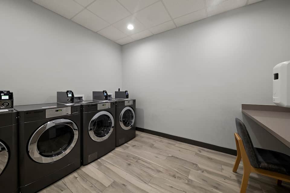 Hotel laundry facility with row of black industrial washing machines and folding counter