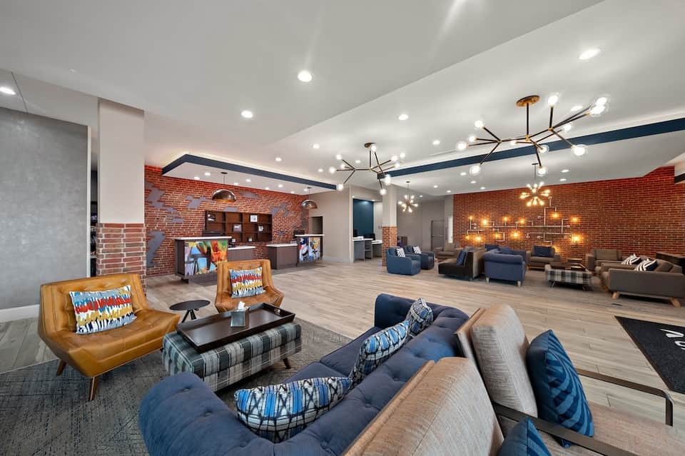Contemporary hotel lobby with exposed brick, blue accents, leather seating, pendant lighting, and lounge areas