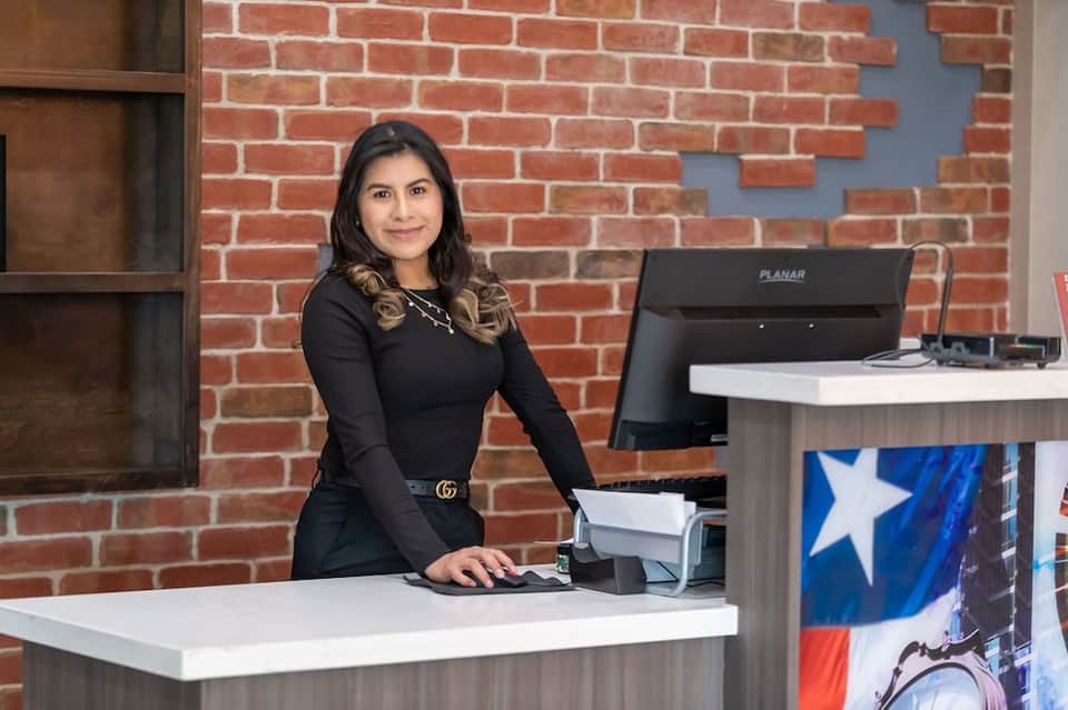Professional woman at hotel front desk with brick wall backdrop and computer terminal