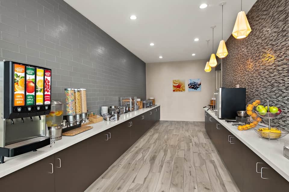 Modern beverage station with juice dispenser, cereal containers, and pendant lighting in bright corridor