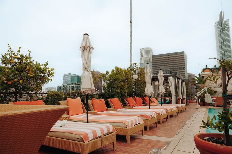 Urban rooftop lounge with orange striped loungers, white umbrellas, and city skyline
