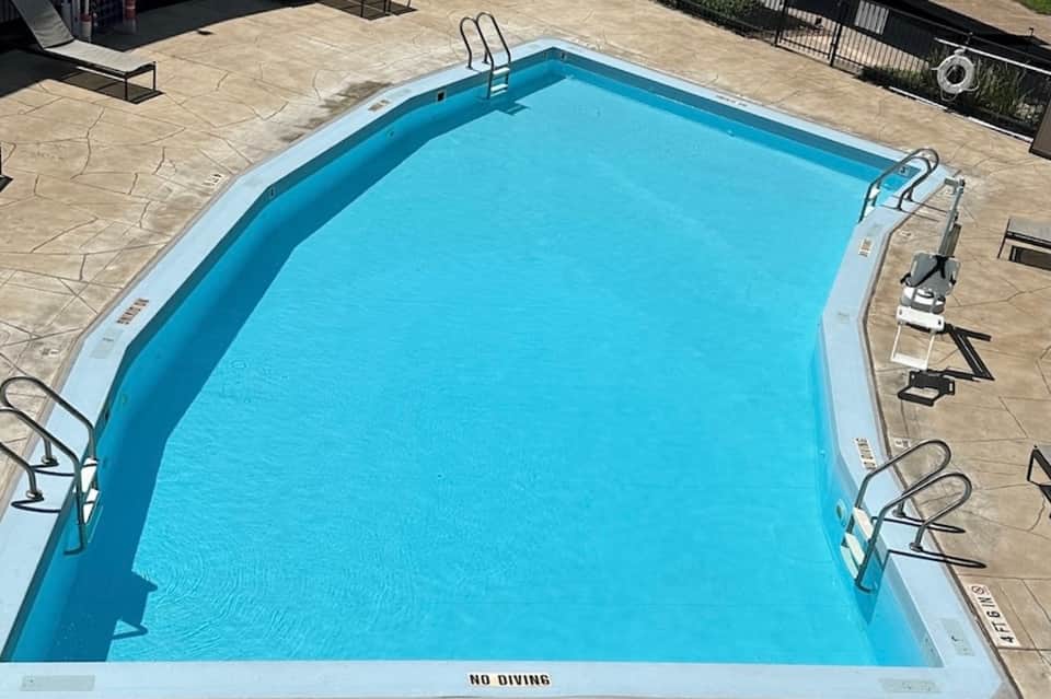 Outdoor swimming pool with clear blue water, lounge chairs, and stone patio deck