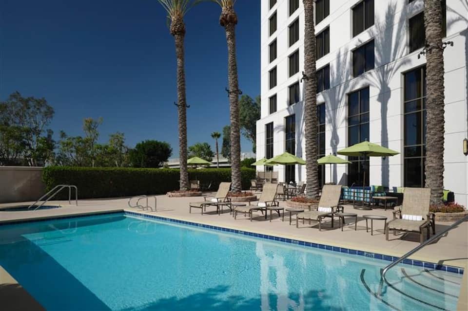 Resort pool with loungers, palm tree shade, and white building facade