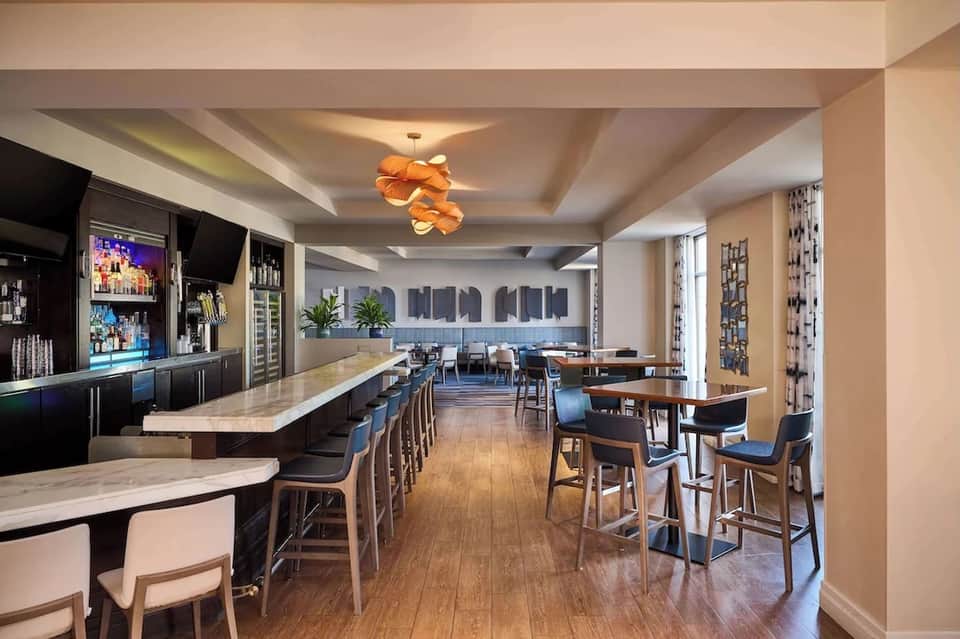 Upscale hotel bar and lounge with stone counters, backlit shelving, and ocean-view windows