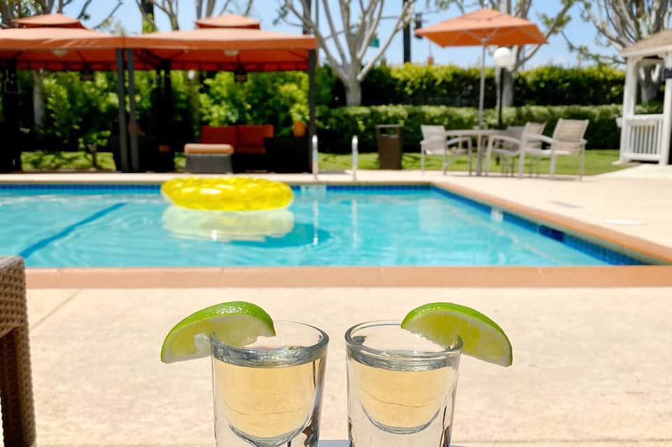 Two shot glasses with lime wedges by pool at resort with yellow float and lounge chairs