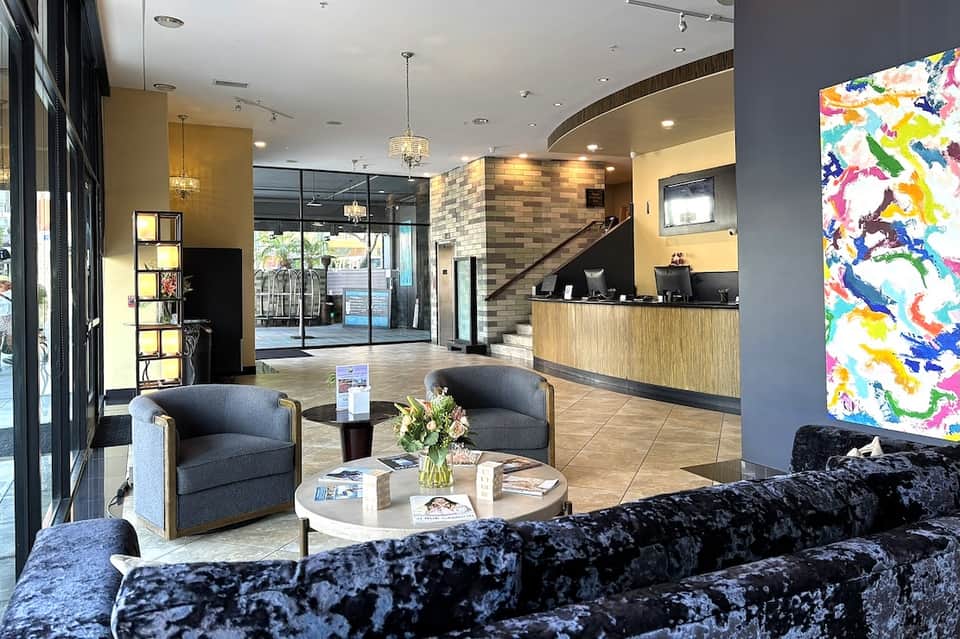 Contemporary hotel lobby with reception desk, seating area, pendant lights, and colorful abstract art