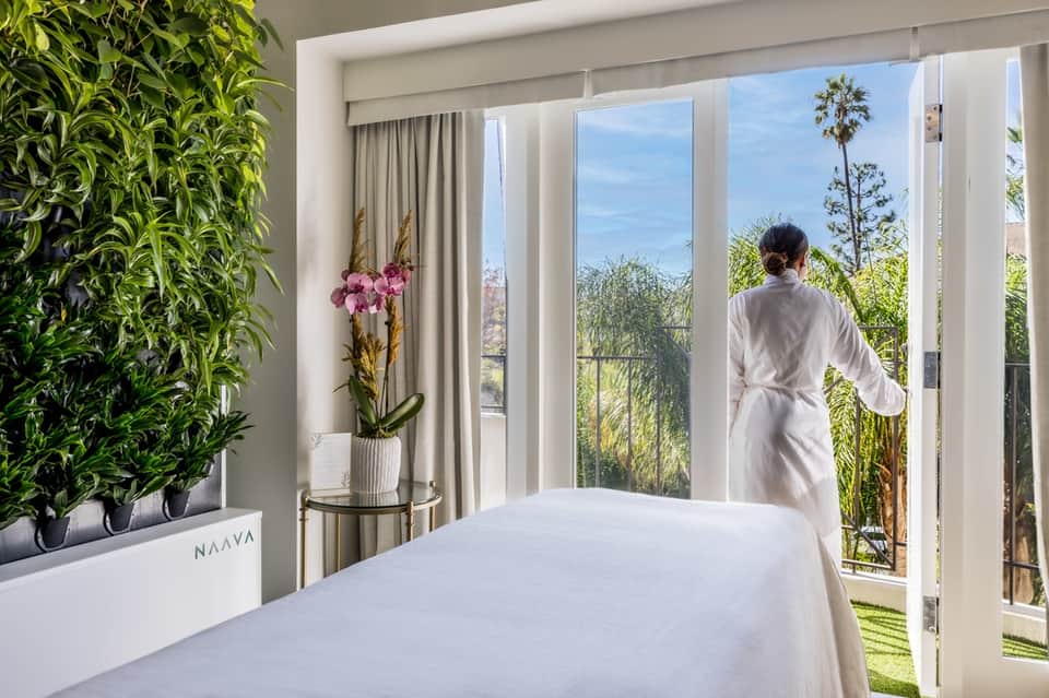 Modern hotel room with balcony overlooking tropical gardens, indoor plant wall, and white bedding