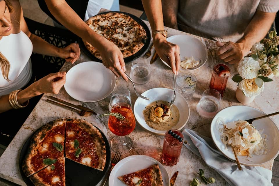 Overhead view of casual outdoor dining with pizza, appetizers, drinks, and fresh flowers on table