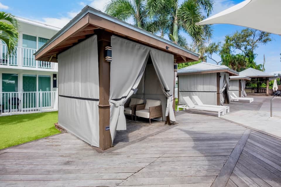 Outdoor cabanas with draped curtains on wooden deck beside residential building and palm trees