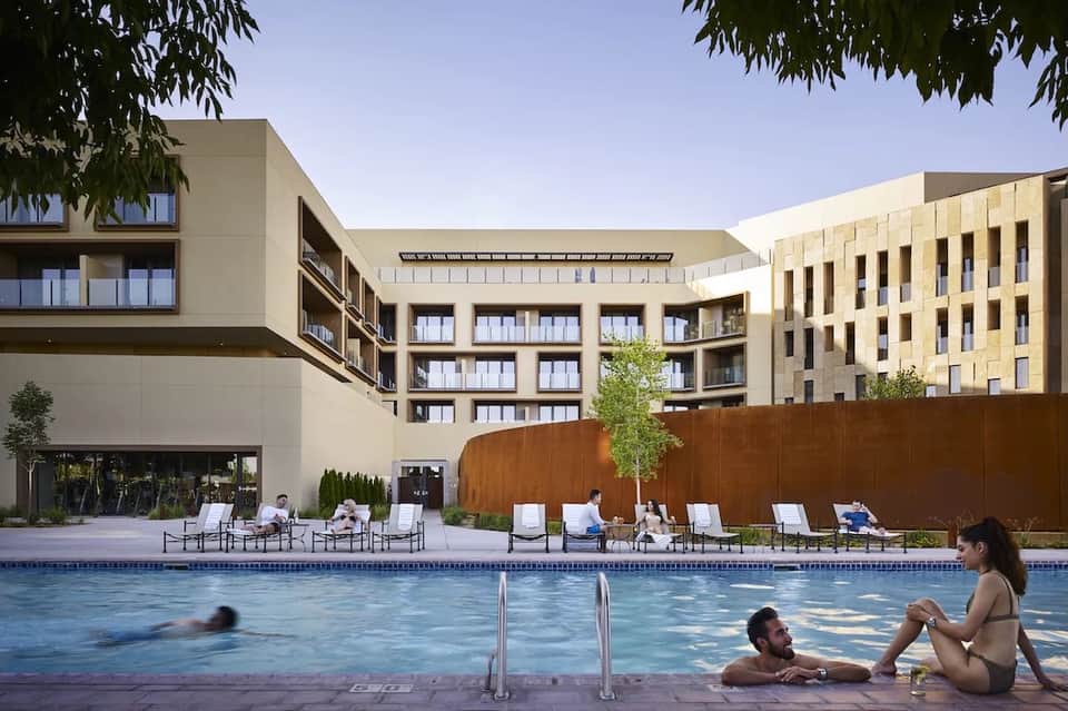 Resort pool with lounge chairs and guests swimming, modern architecture backdrop